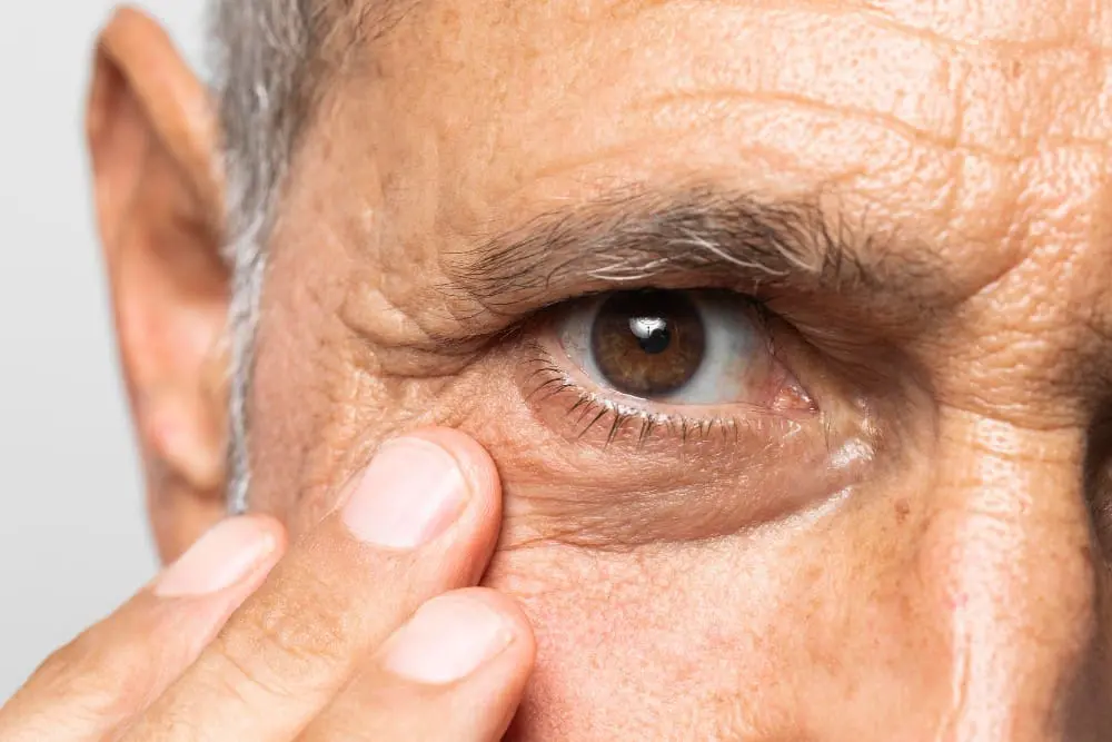 Close-up of an elderly person's eye with visible wrinkles, and a hand gently touching the face at Eye Care Clinic.