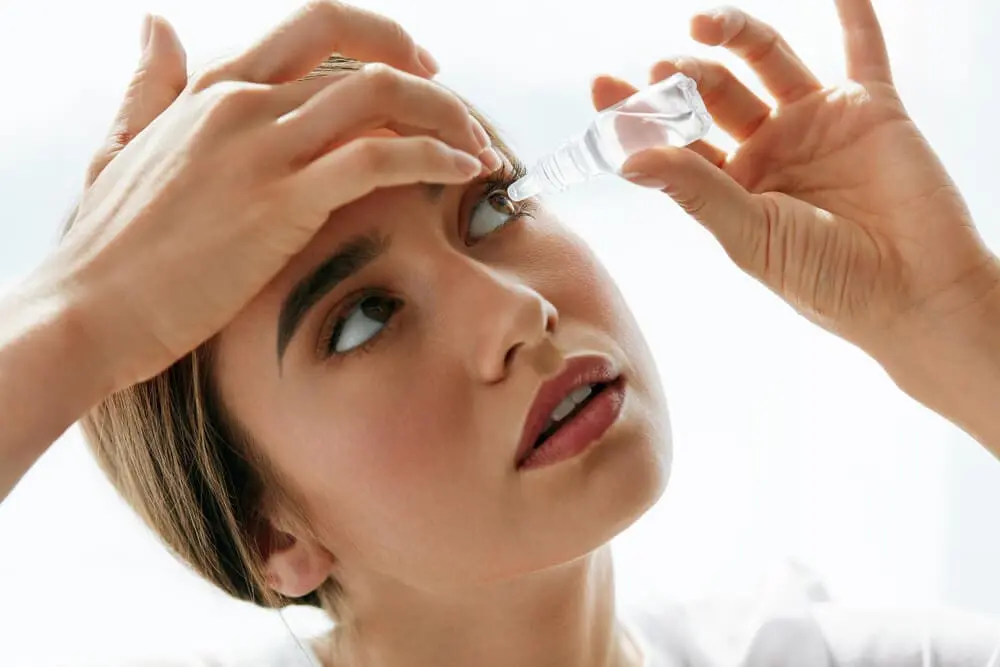 Woman applying eye drops at Eye Care Clinic.